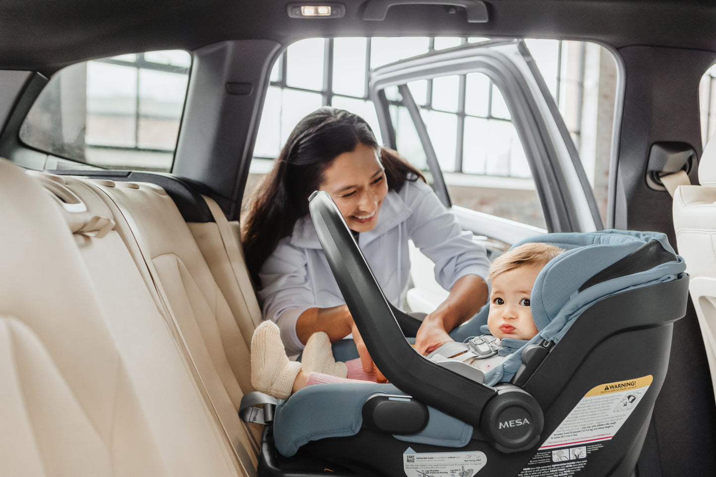 Woman adjusting a uppababy baby car seat with a baby doll inside a vehicle.
