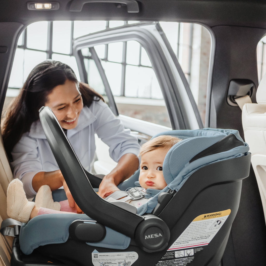 Woman adjusting a uppababy baby car seat with a baby doll inside a vehicle.