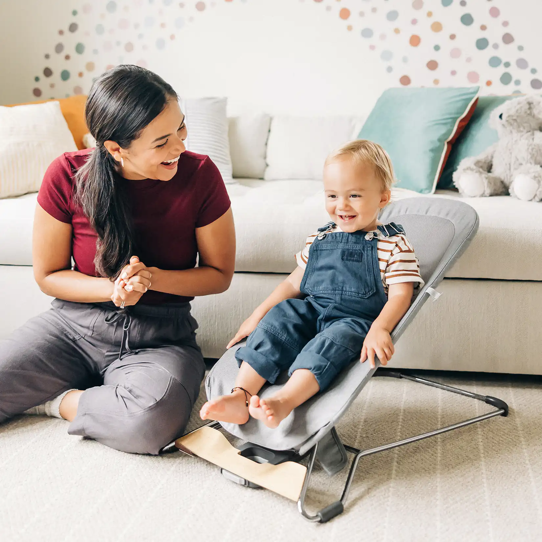 Young child seated in a reclining baby bouncer with caregiver nearby