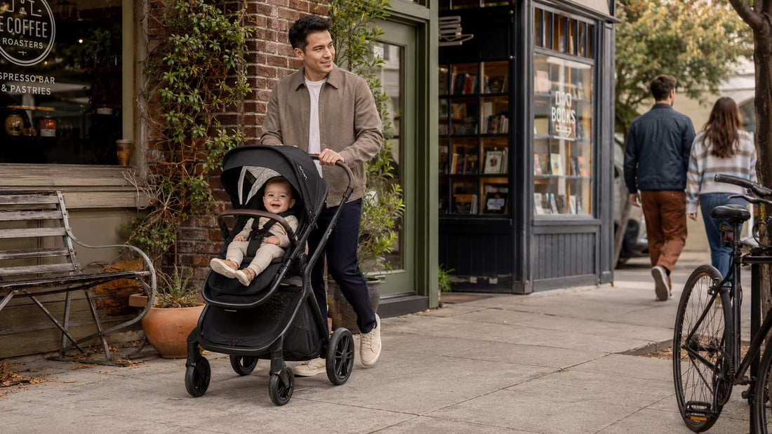 A father walking past city shops with his baby in a black Nuna DEMI Icon stroller.