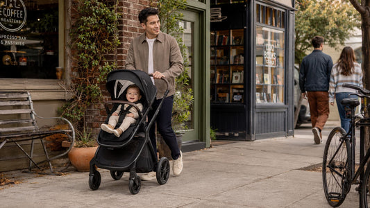 A father walking past city shops with his baby in a black Nuna DEMI Icon stroller.