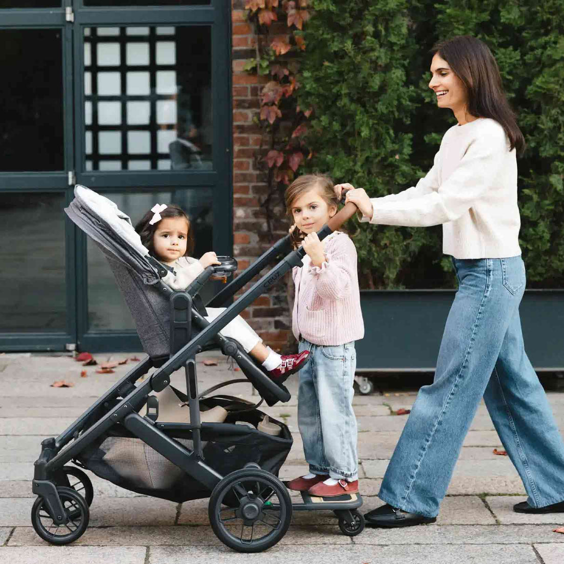 Woman pushing a stroller with two children outdoors.