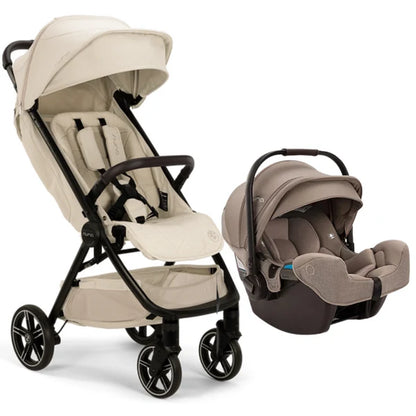 
A stroller and infant car seat travel system in warm beige and taupe tones with black frames, shown on a clean white background. The stroller features a large canopy, padded seat, and storage basket, while the matching car seat is positioned beside it.