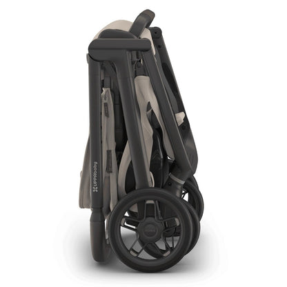 
Side profile of a folded beige and grey UPPAbaby stroller standing upright on a white background.