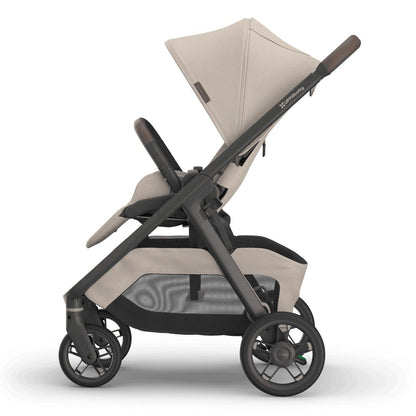
Side profile of a beige baby stroller with a grey frame, sun canopy, and storage basket, isolated on a white background.