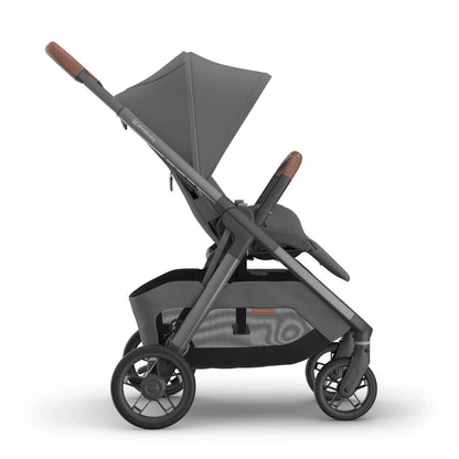 
Side profile of a grey forward-facing baby stroller with an extended sun canopy and brown leather handle grips, isolated on a white background.