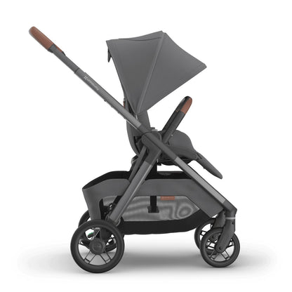
Side profile of a grey parent-facing baby stroller with an extended sun canopy and brown leather handle grips, isolated on a white background.