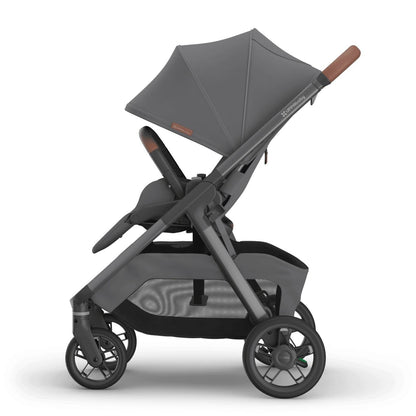 
Side profile of an upright grey forward-facing baby stroller with an extended sun canopy and brown leather handle grips, isolated on a white background.