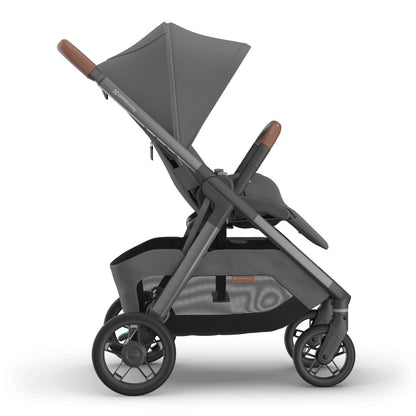 
Side profile of an upright grey forward-facing baby stroller with an extended sun canopy and brown leather handle grips, isolated on a white background.