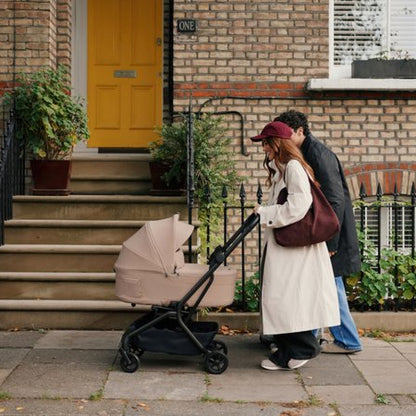 Two people walking with a baby stroller in front of a brick building with a yellow door.