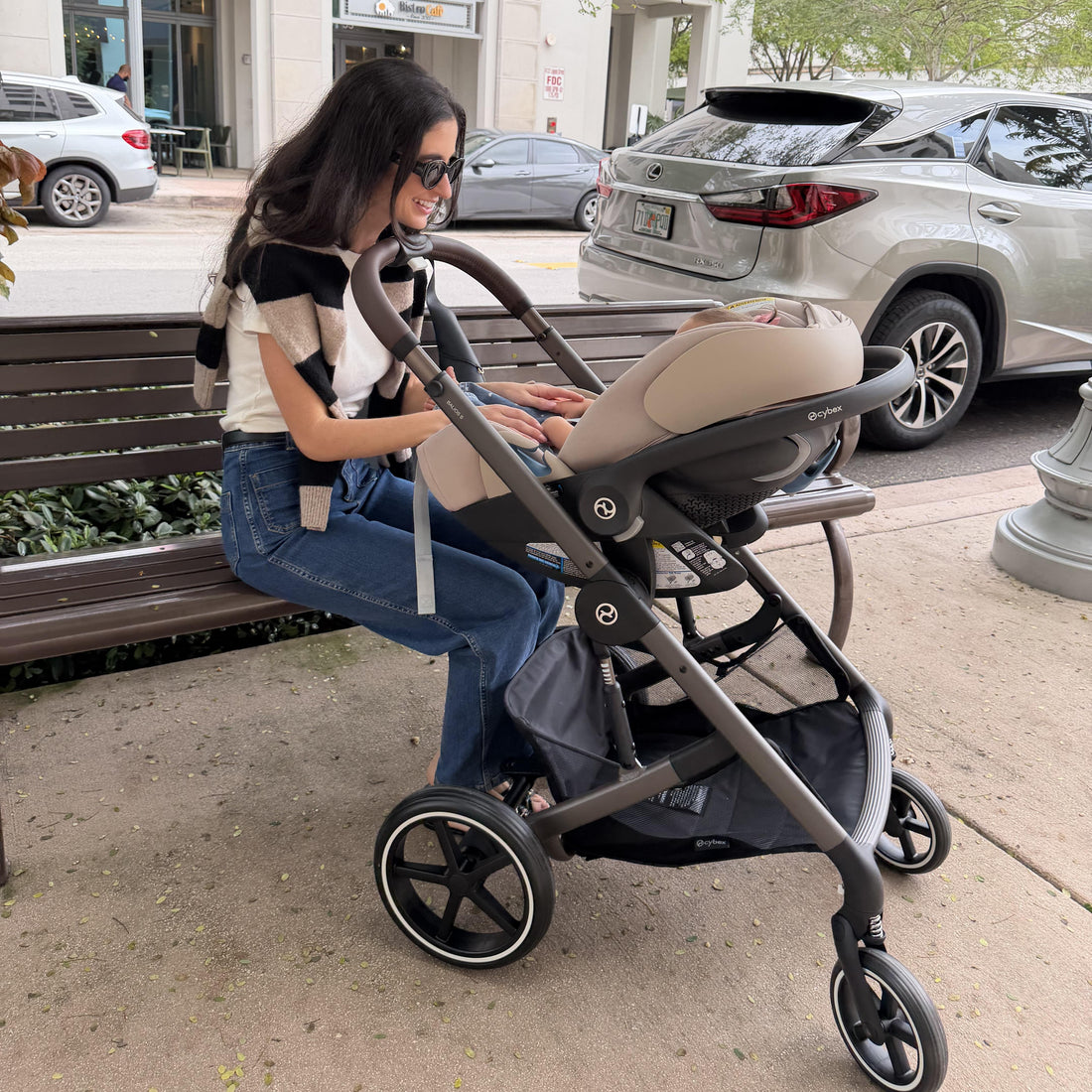 Woman sitting on a bench with a stroller and baby seat in an urban setting