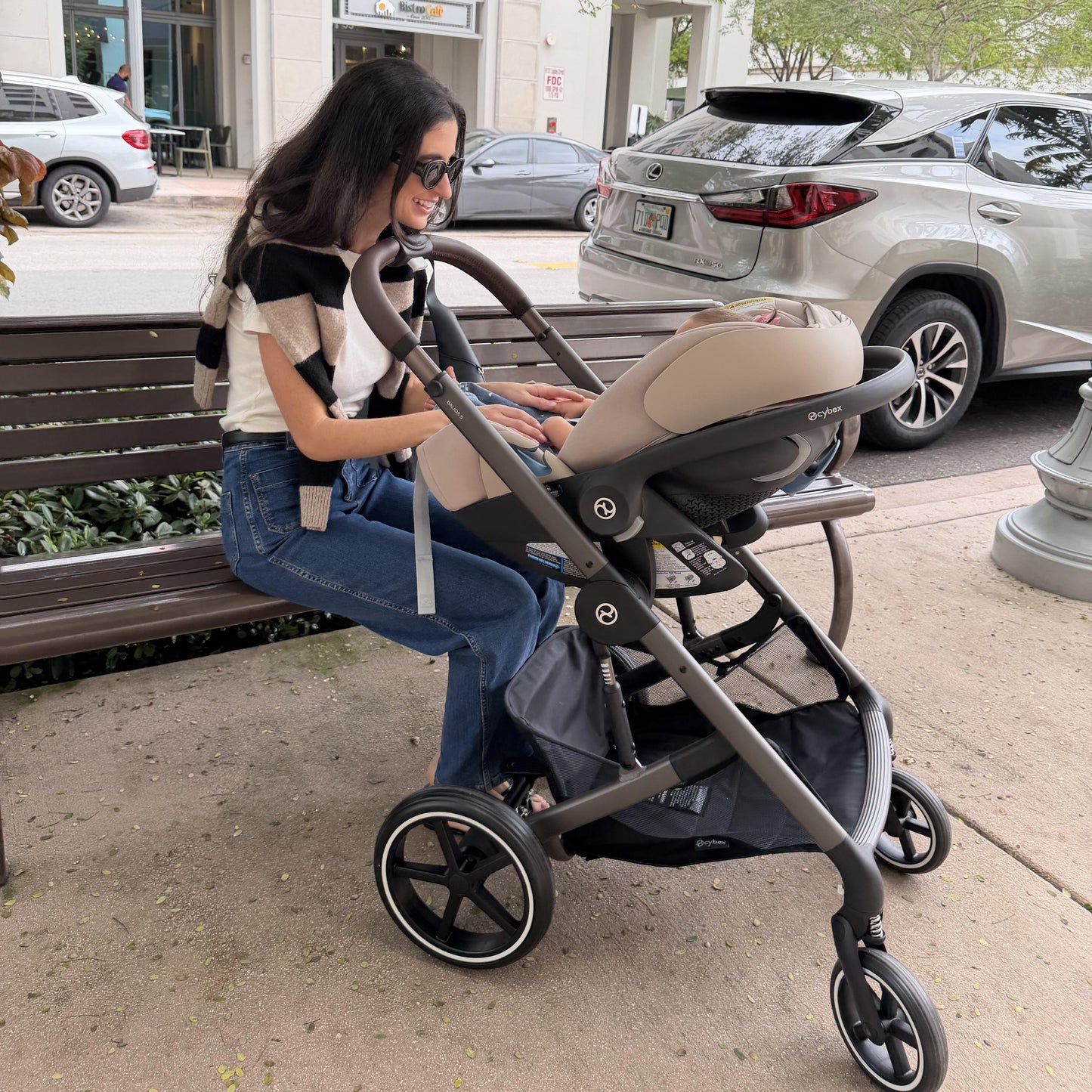 Woman sitting on a bench with a stroller and baby seat in an urban setting