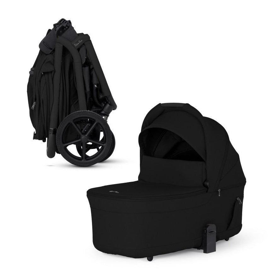 A compactly folded all-black stroller frame standing next to its matching standalone bassinet.