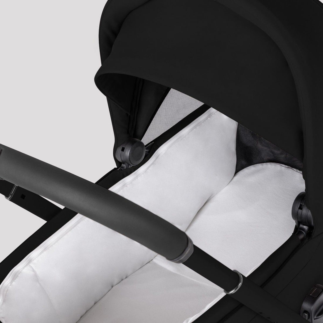 Close-up view into a black stroller bassinet showing a soft, white padded mattress lining.