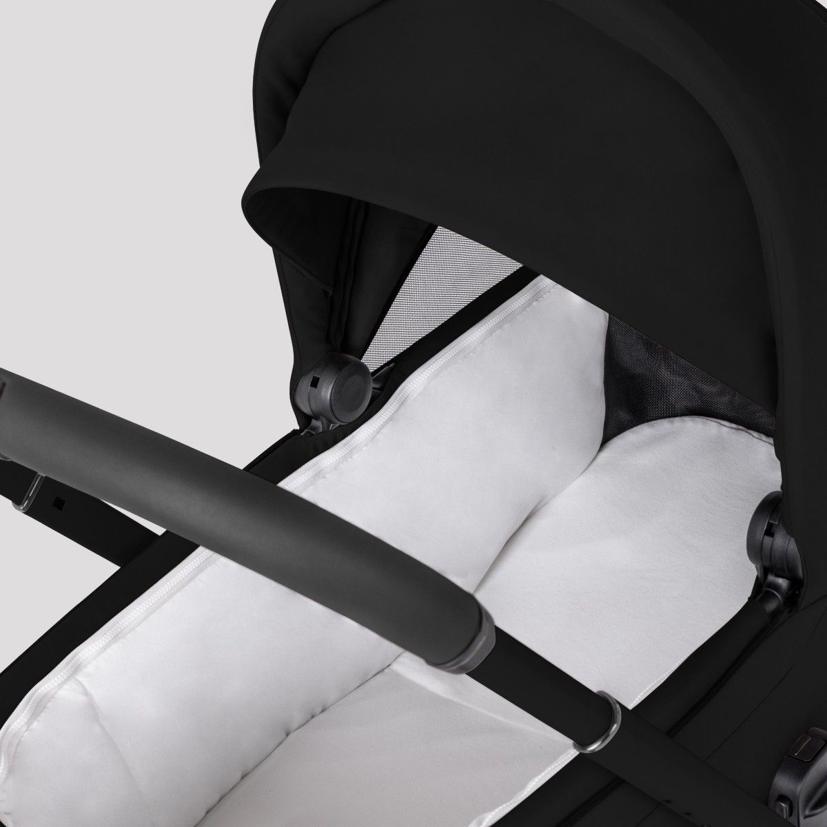 Close-up view into a black stroller bassinet showing a soft, white padded mattress lining.