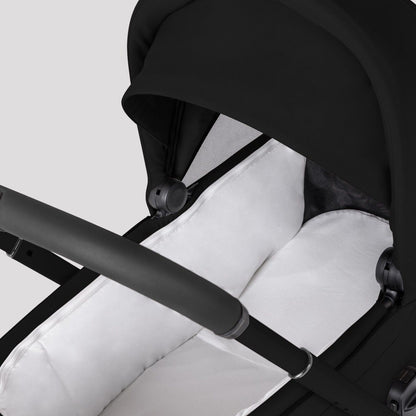 A close-up view looking into a black stroller bassinet with a white padded lining and mattress.