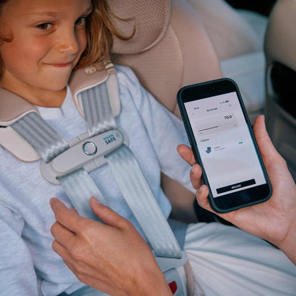 Child in a callisto car seat with a smartphone displaying an sensorsafe app, held by an adult.