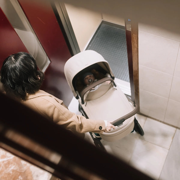 Joolz Hub² Compact Lightweight Stroller with Newborn Carry Cot in Sandy Taupe Inside Elevator Lifestyle