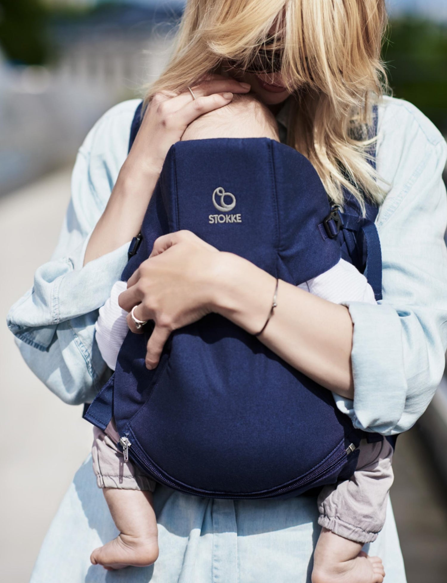 Woman bonding with a baby while using a Stokke baby carrier outdoors.