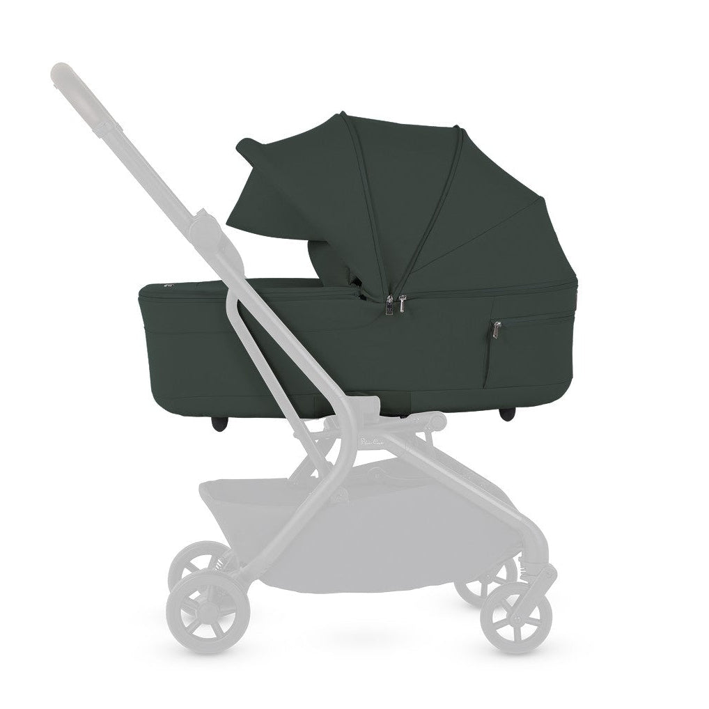A side view diagram of a stroller highlighting the attached olive green bassinet with the chassis faded out.