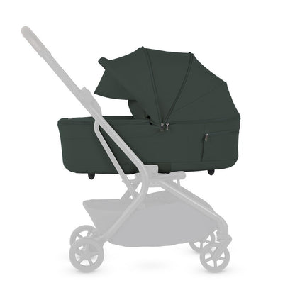 A side view diagram of a stroller highlighting the attached olive green bassinet with the chassis faded out.