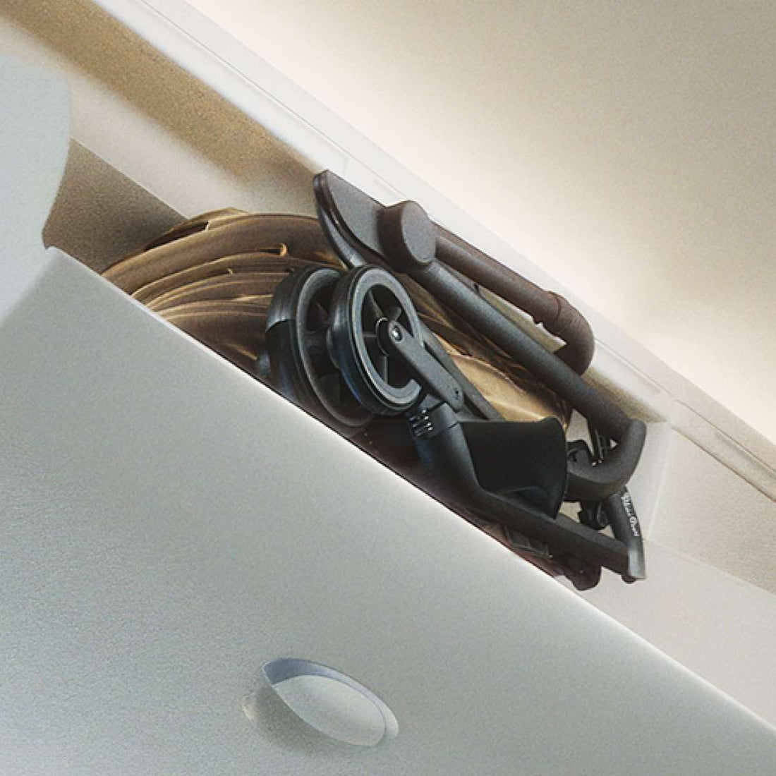 A compactly folded stroller stored inside an airplane overhead bin.