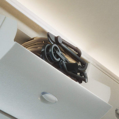 A compactly folded stroller stored inside an airplane overhead bin.
