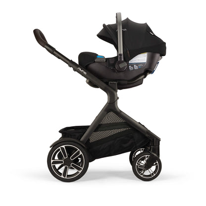 
A black and dark gray stroller with an attached infant car seat and canopy, shown from a side profile on a clean white background. The stroller features a large storage basket underneath and multi-spoke wheels.