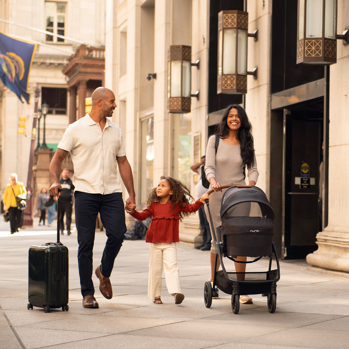 
Family strolling baby with Nuna Triv & Swiv series Bassinet with little girl between mom and dad