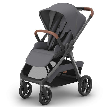 A modern stroller in dark gray fabric with brown leather-look handlebar grips and a dark gray frame, shown at a three-quarter angle on a clean white background.