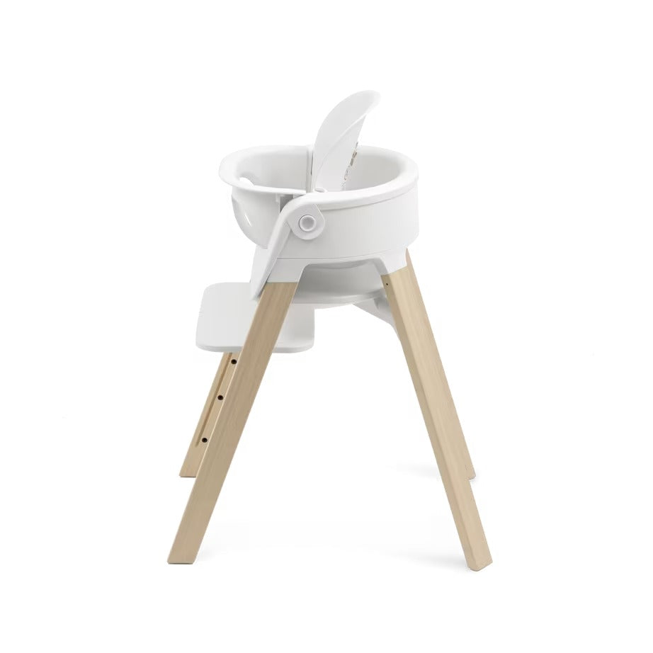 
A modern high chair with a white molded plastic seat and light natural wood legs, shown from a three-quarters angle on a solid white background.