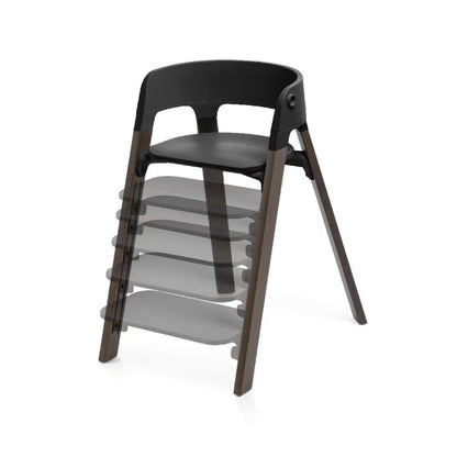 
A modern wooden dining chair with a black molded seat and backrest, shown on a clean white background. A semi-transparent layered graphic behind it illustrates additional seat heights or configurations.