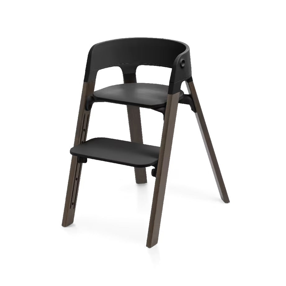 
A modern step stool chair with a matte black plastic seat, backrest, and footrest, supported by four dark brown wooden legs, shown on a clean white background.