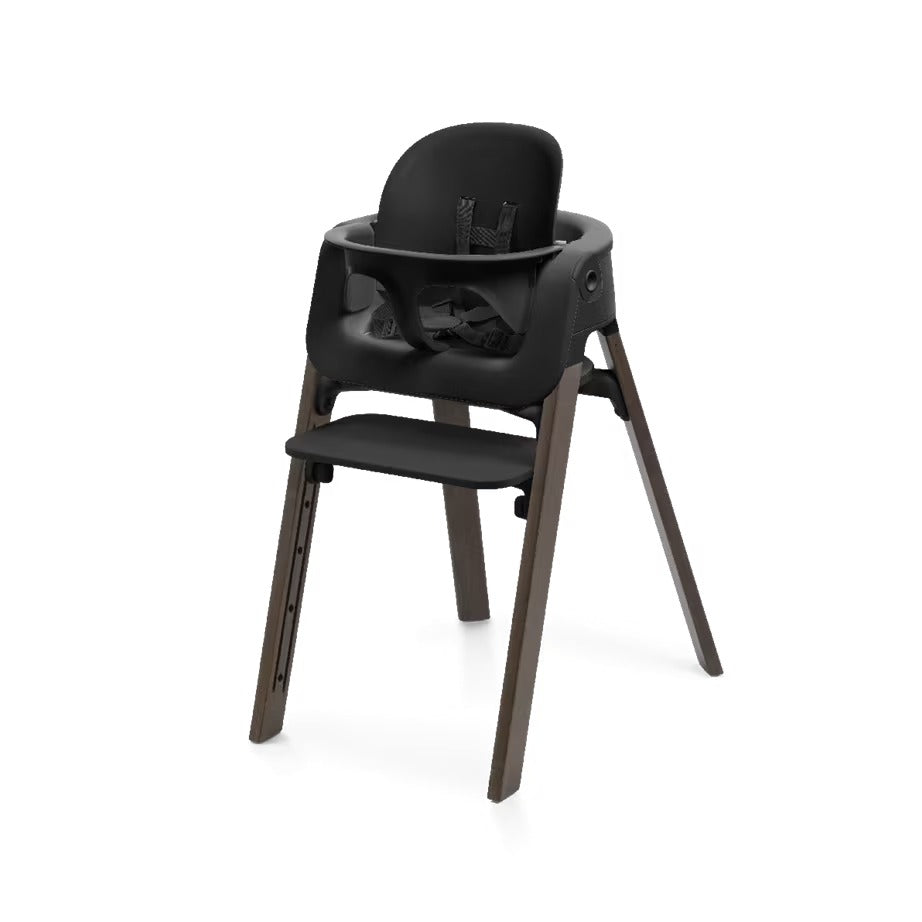 
A modern high chair with a black molded plastic seat, backrest, and tray, supported by four tapered dark brown wooden legs, shown on a plain white background.