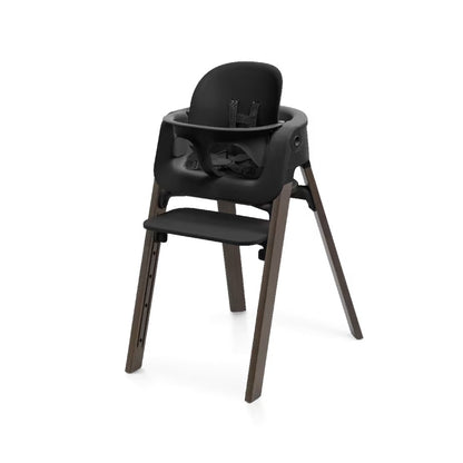 
A modern high chair with a black molded plastic seat, backrest, and tray, supported by four tapered dark brown wooden legs, shown on a plain white background.