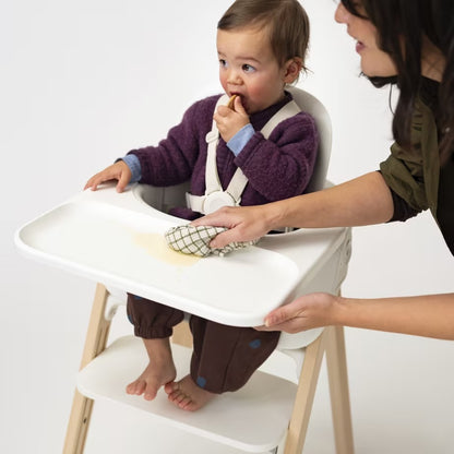 
Child in a high chair being fed by an adult on a white background