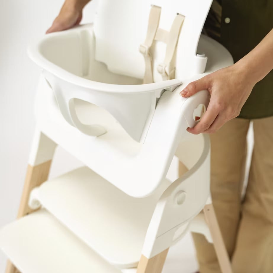 
White high chair with beige straps being held by a person