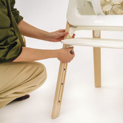 
Person assembling a white and wooden high chair on a white background