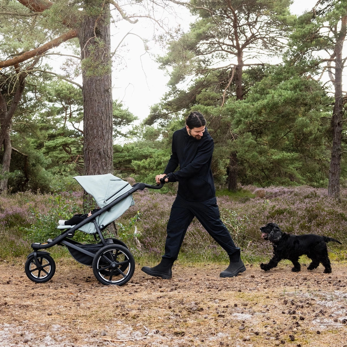 Thule Urban Glide on unmarked path outdoors with Dad, baby, and puppy out on an adventure with all-terrain wheels, canopy for protection and more