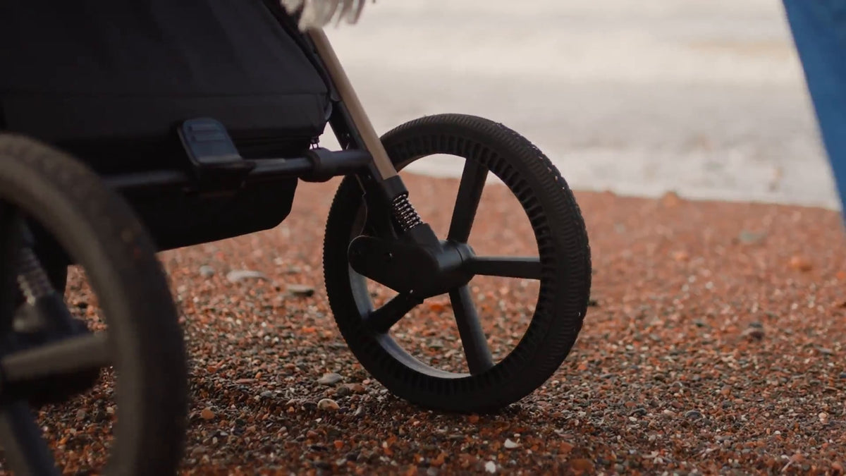 Close-up of the Silver Cross Cove 2 stroller's oversized RideTech wheels and suspension system on a gravel surface.
