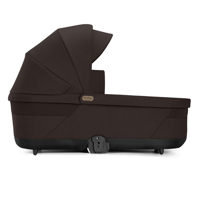 
A dark brown baby bassinet with a matching canopy, shown from a side profile view on a clean white background. The brand name 'Cybex' is visible on a small gold badge on the side of the bassinet.