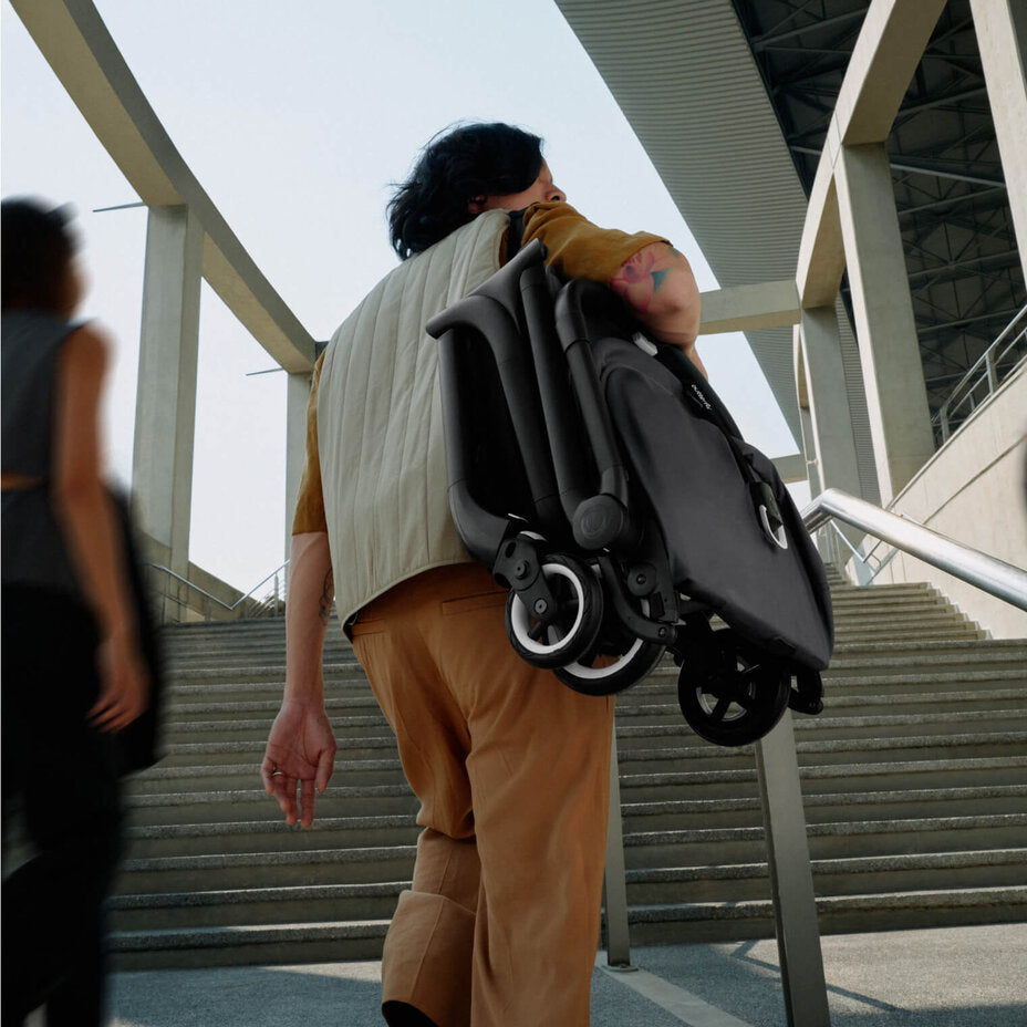 Person carrying a folded Bugaboo stroller up a flight of stairs.
