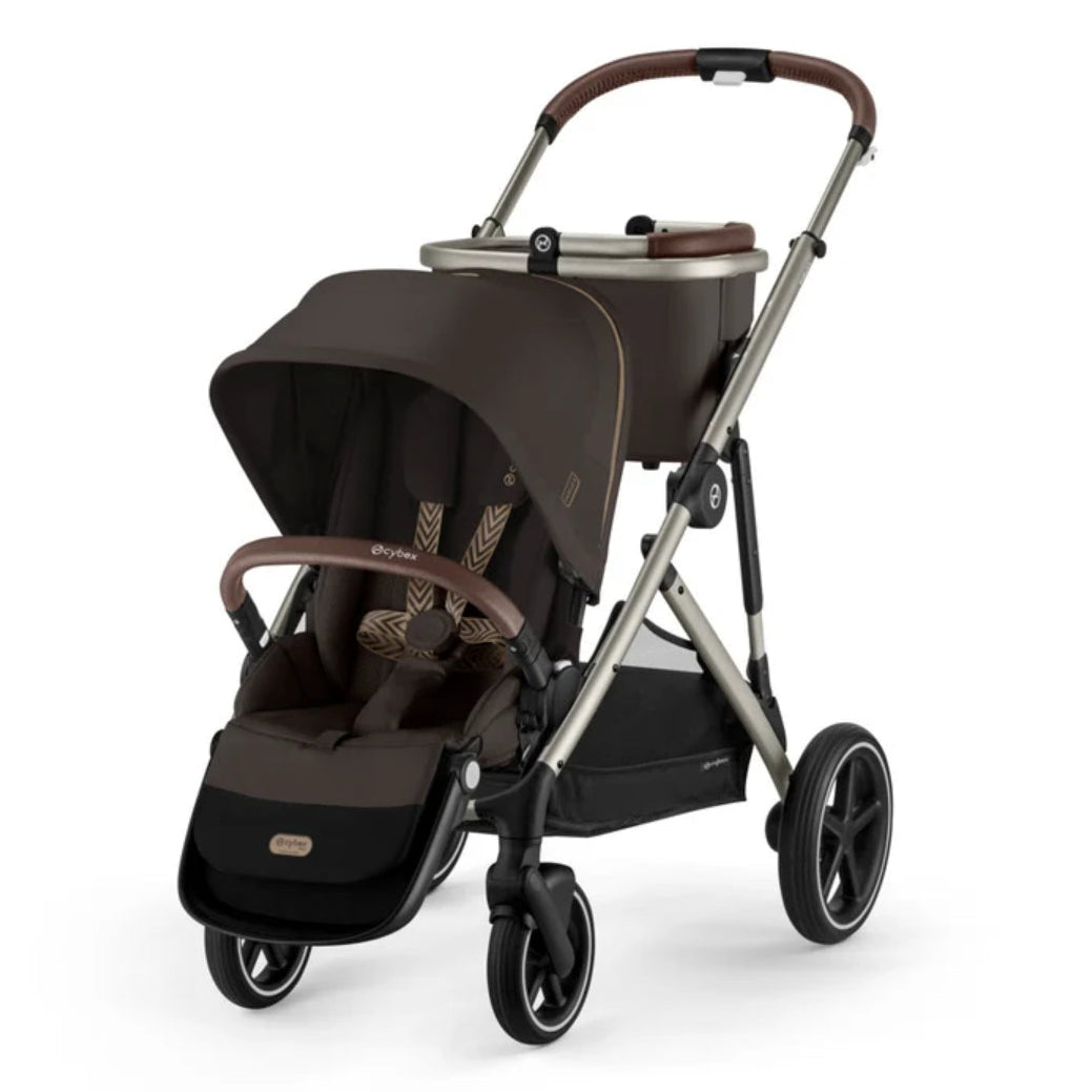 A premium stroller and bassinet travel system in dark brown and silver, shown from a three-quarter angle on a white background. The stroller features a dark brown canopy, matching seat liner, brown leatherette handlebar grips, a silver aluminum frame, and a matching bassinet attachment on top.