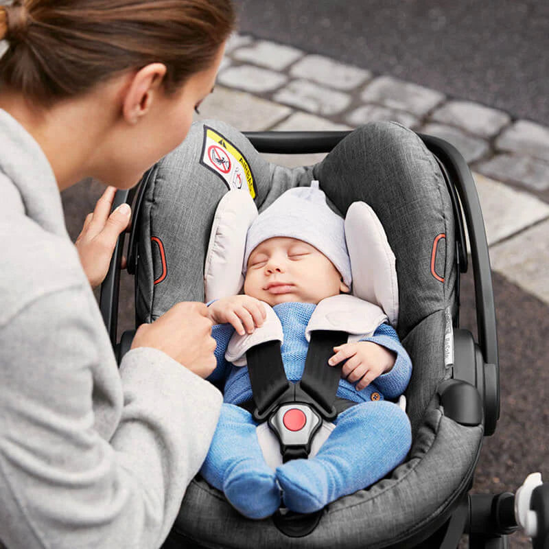 Woman caring for a sleeping baby in a Stokke infant car seat.