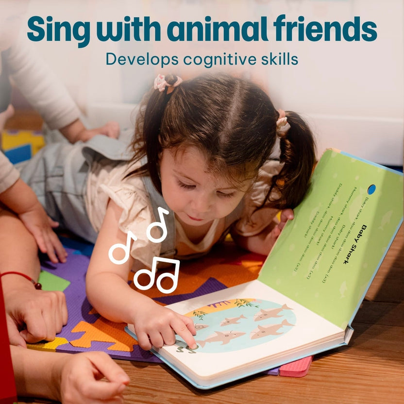 
A young child lies on a colorful floor mat reading a children's book with a song, while another person assists nearby. Large text at the top reads 'Sing with animal friends' and 'Develops cognitive skills.