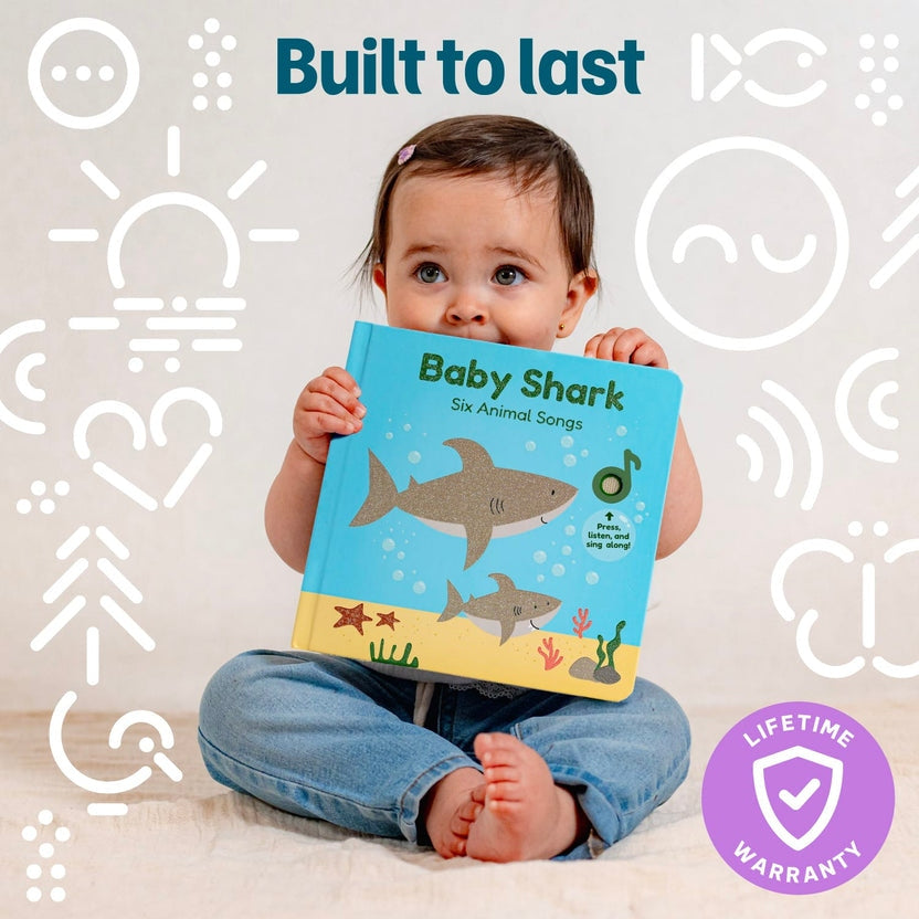 
A baby sitting cross-legged and holding a blue interactive sound book titled "Baby Shark - Six Animal Songs".