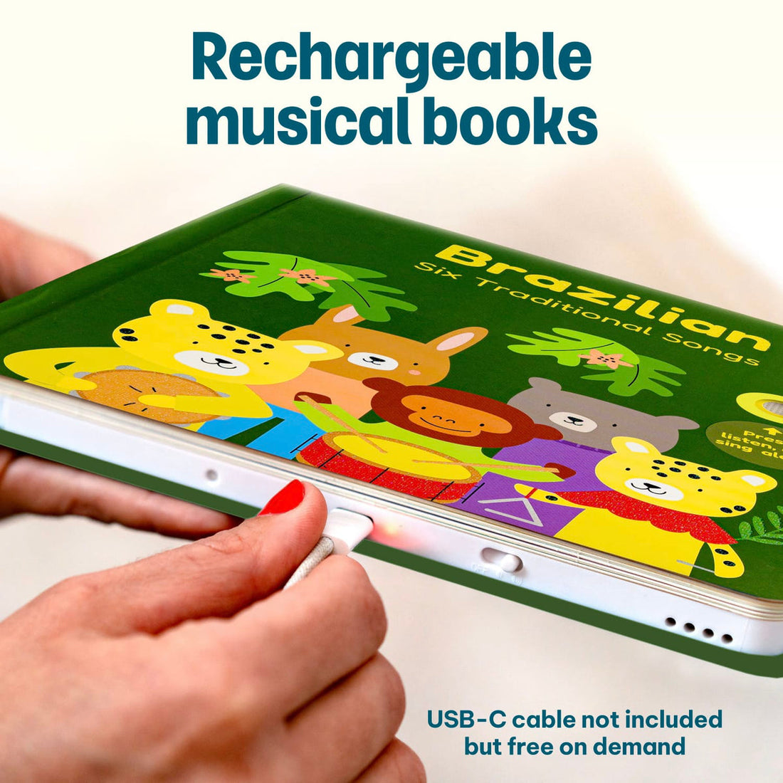 
A hand holds a green children's music book with cartoon animals on the cover, charging it with a USB-C cable. Text on the image reads 'Rechargeable musical books' and 'USB-C cable not included but free on demand'.