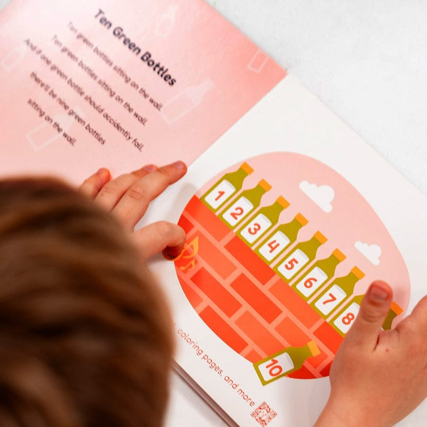 
A child holding open a book showing the song lyrics and illustrations for *"Ten Green Bottles"*.