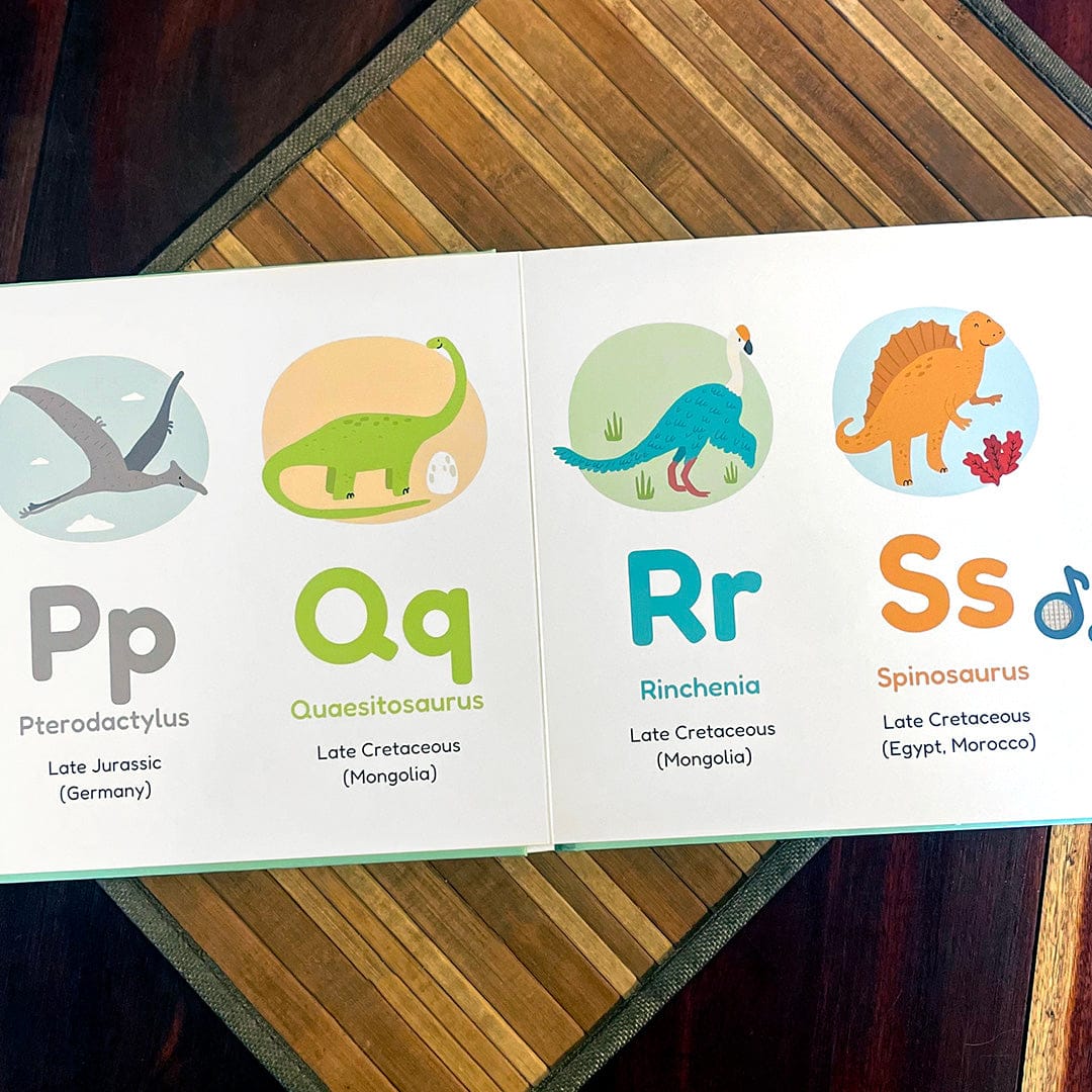 
An open children's educational book showing the letters P, Q, R, and S with dinosaur illustrations and names, placed on a striped wooden surface.