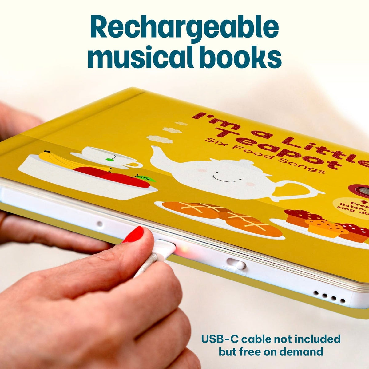 
A close-up of a person's hand plugging a USB-C cable into a white electronic musical book with a yellow cover that reads 'I'm a Little Teapot Six Food Songs.' Large text says 'Rechargeable musical books,' and smaller text says 'USB-C cable not included but free on demand.